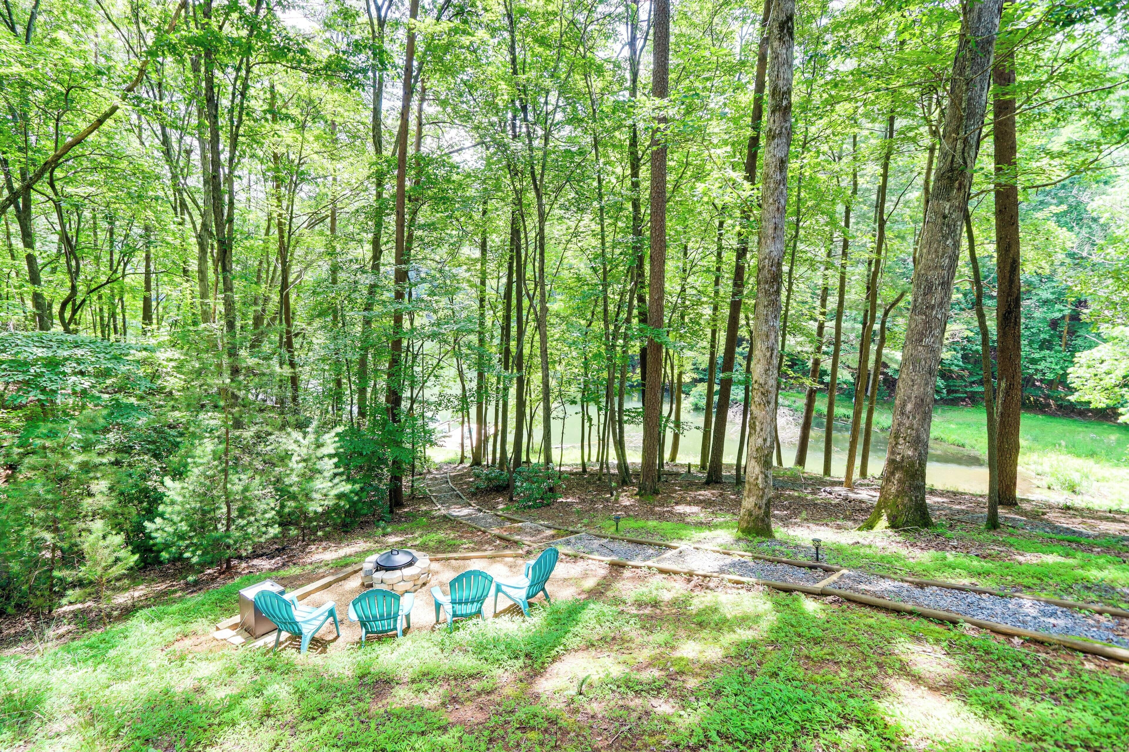 A forested area with a seating arrangement including chairs and a fire pit.