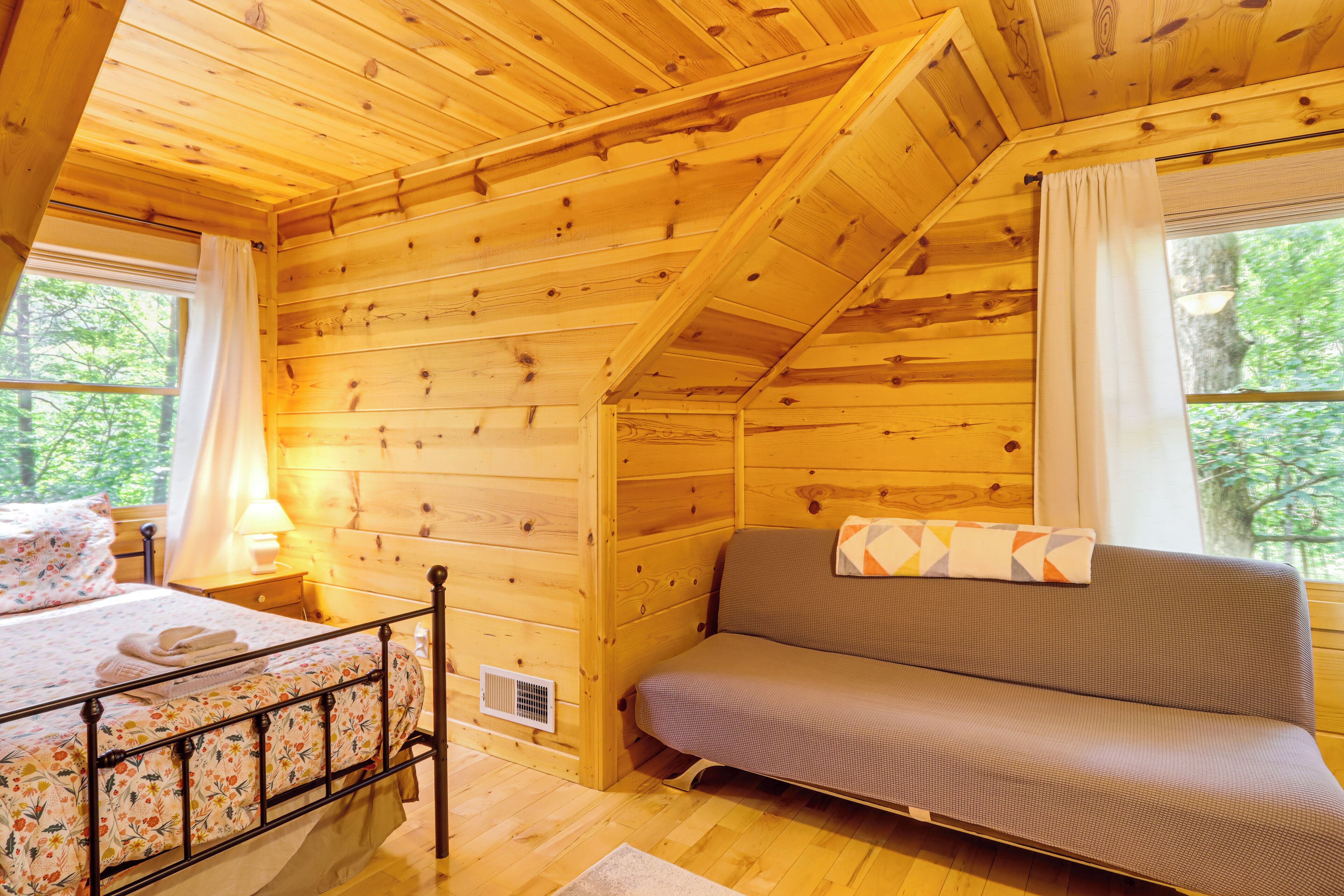 Une pièce de cabane en bois comprenant un lit, un canapé, une fenêtre et une lampe.