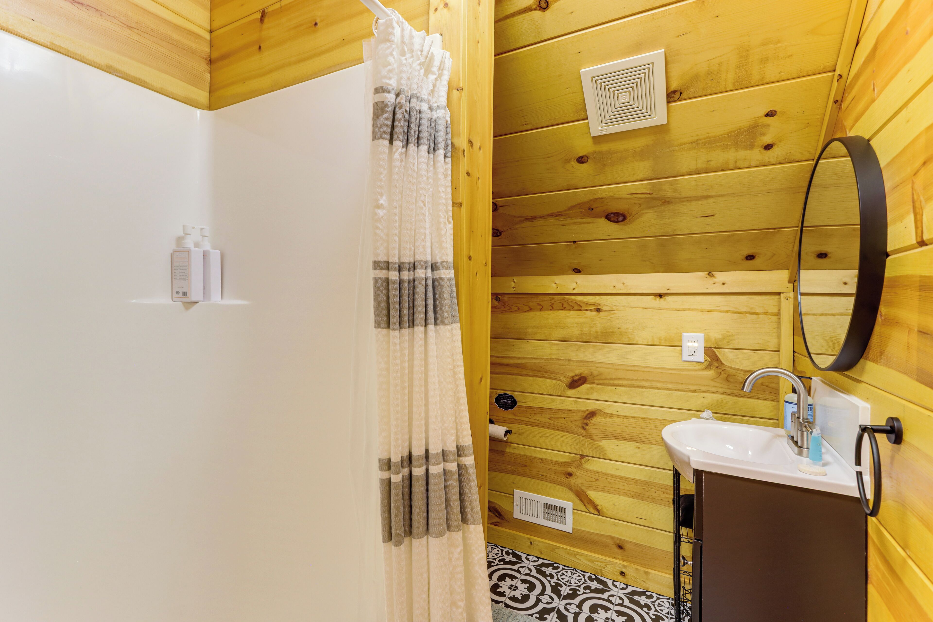 A wooden-paneled bathroom with a shower curtain, a sink with a mirror, and a patterned floor.