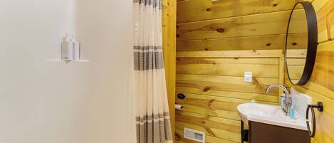 A wooden-paneled bathroom with a shower curtain, a sink with a mirror, and a patterned floor.