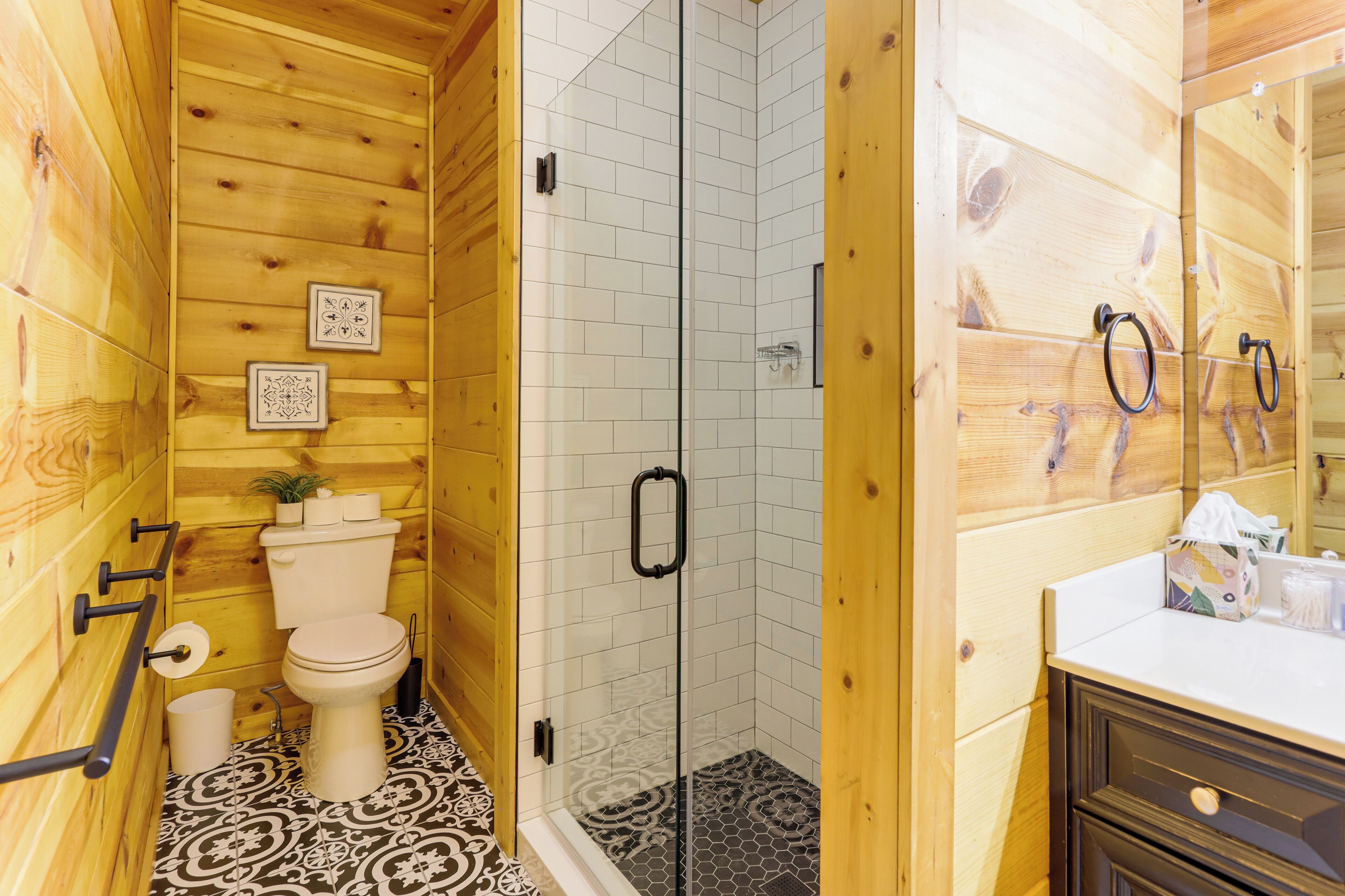 A wooden cabin bathroom with a toilet, a shower with glass doors, and a vanity with a mirror.