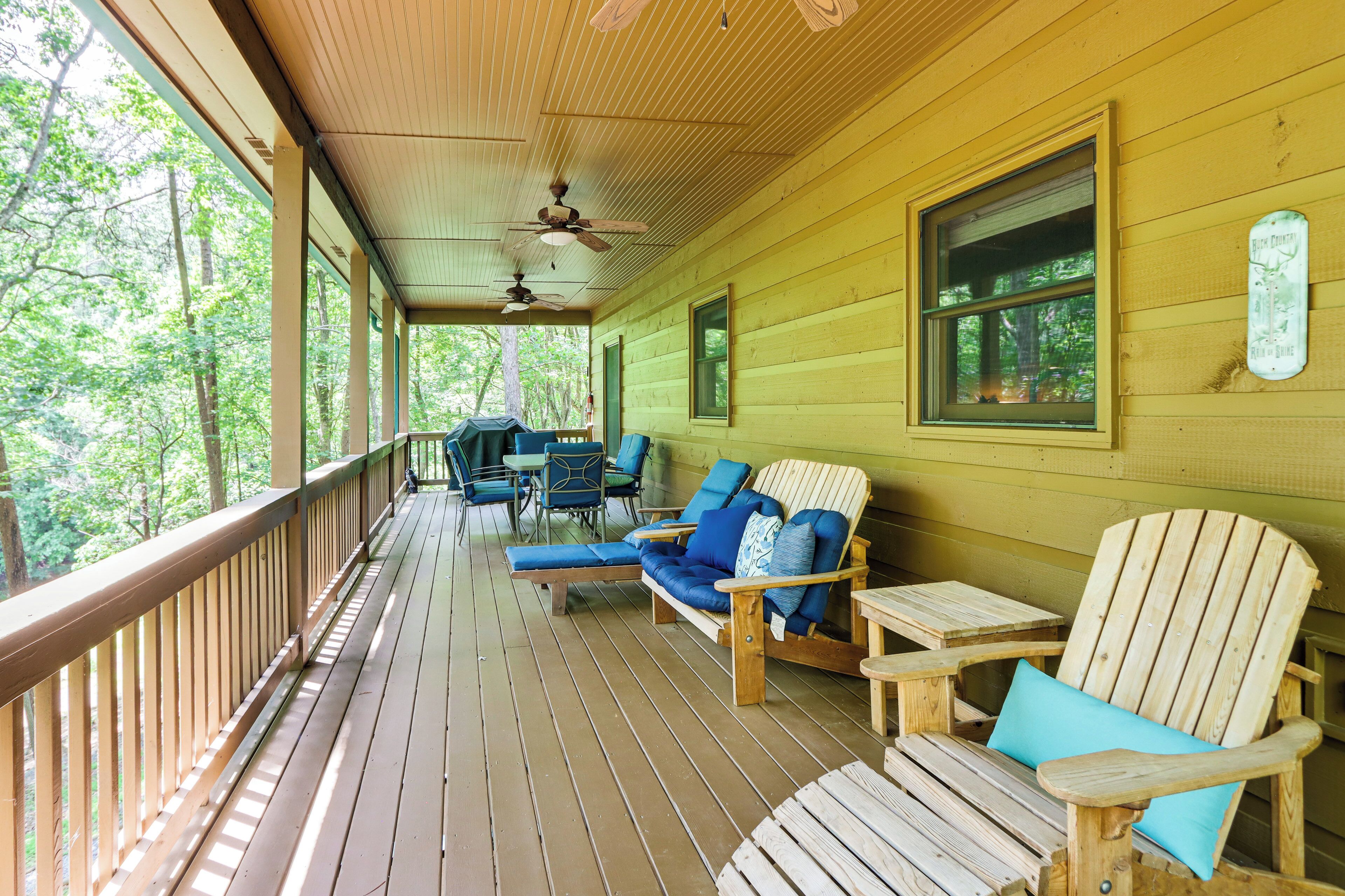 Una terraza de madera con mobiliario exterior, incluyendo sillas y una mesa, con vistas a una zona boscosa.