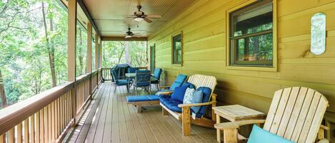 Una terraza de madera con mobiliario exterior, incluyendo sillas y una mesa, con vistas a una zona boscosa.