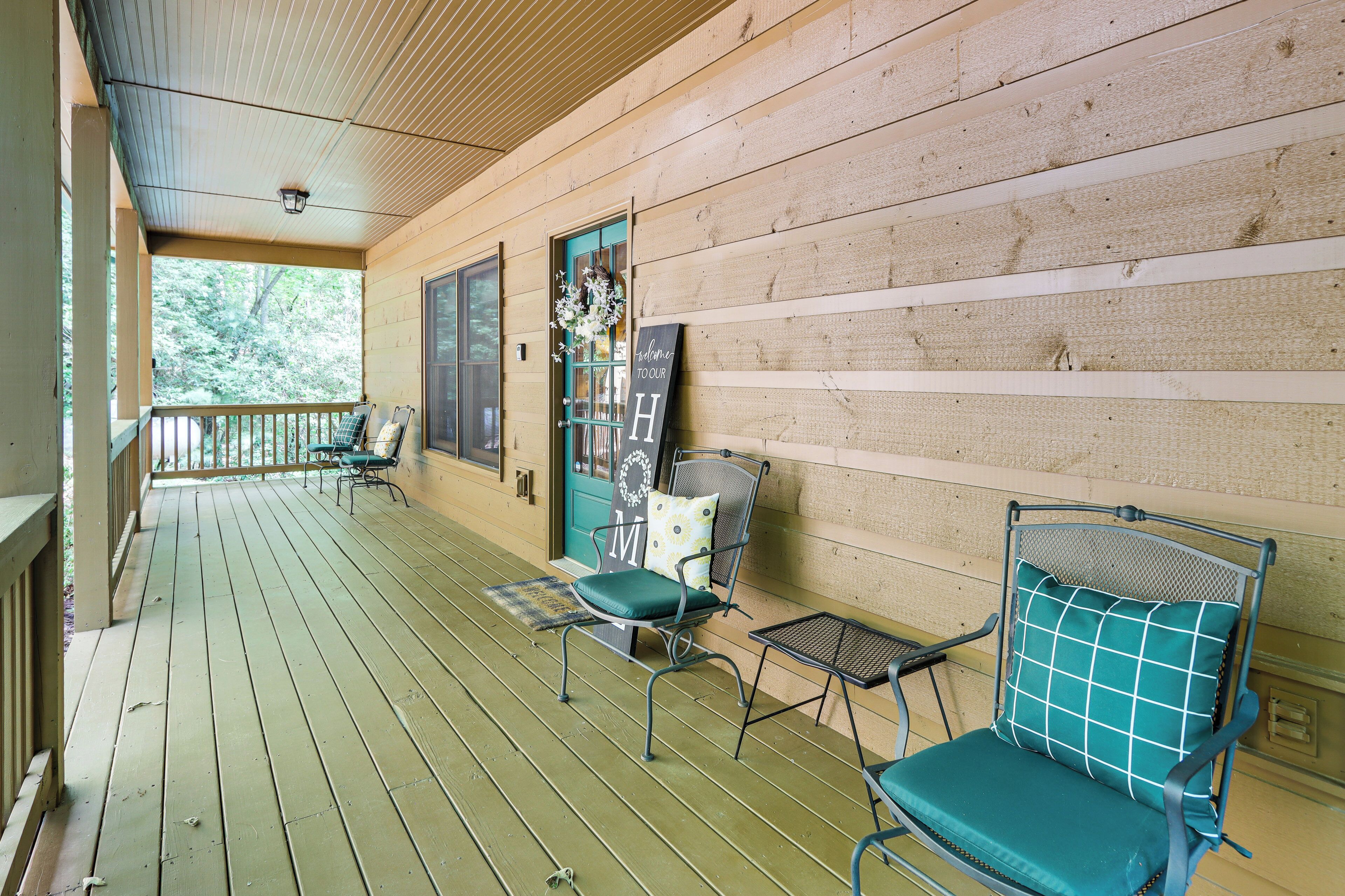 A wooden porch with two chairs and a bench, a door with a 'Welcome to Tour H' sign, and a view of trees through the windows.