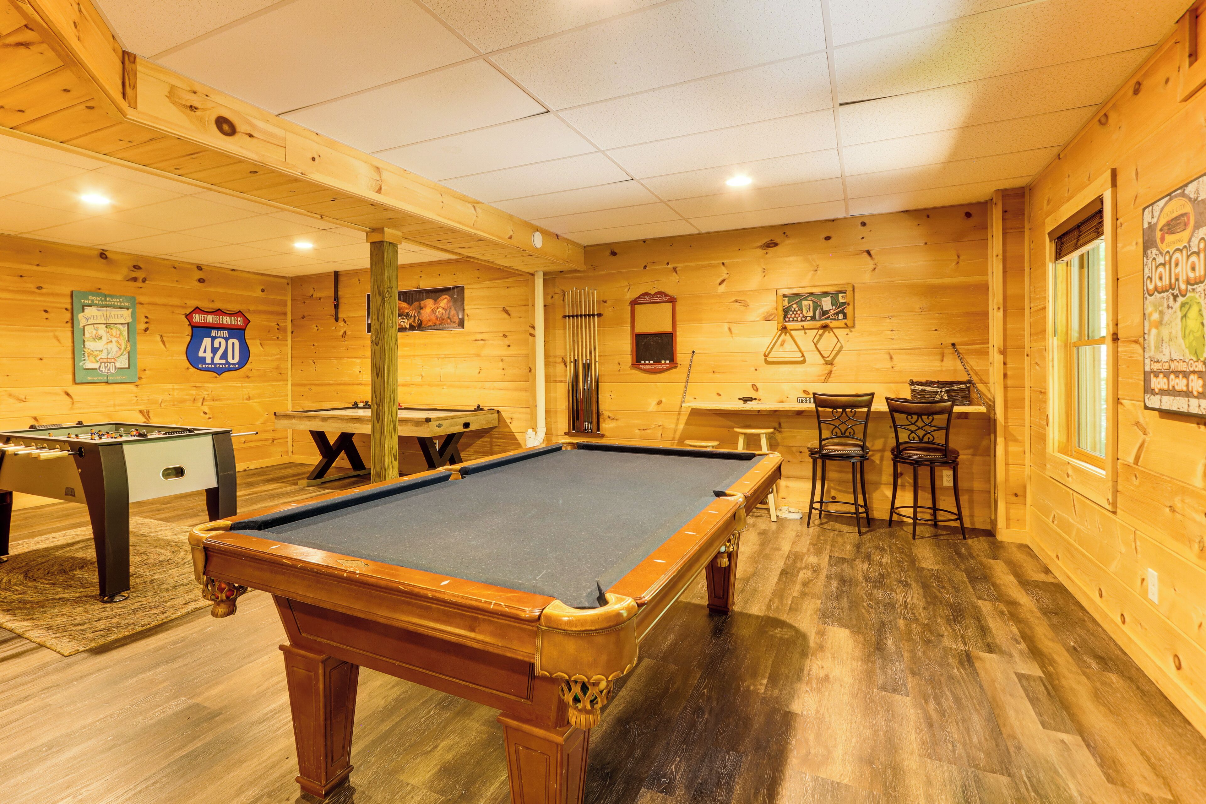 A pool table in a wooden room with a foosball table and a billiards table.