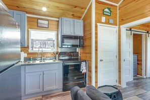 A compact kitchen with grey cabinets, a microwave, an oven, and a refrigerator. - Peaceful Deck & Pool Access! Blue Ridge Tiny Home (Morganton)