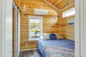 A bedroom with a bed, a window, and an air conditioning unit. - Peaceful Deck & Pool Access! Blue Ridge Tiny Home (Morganton)