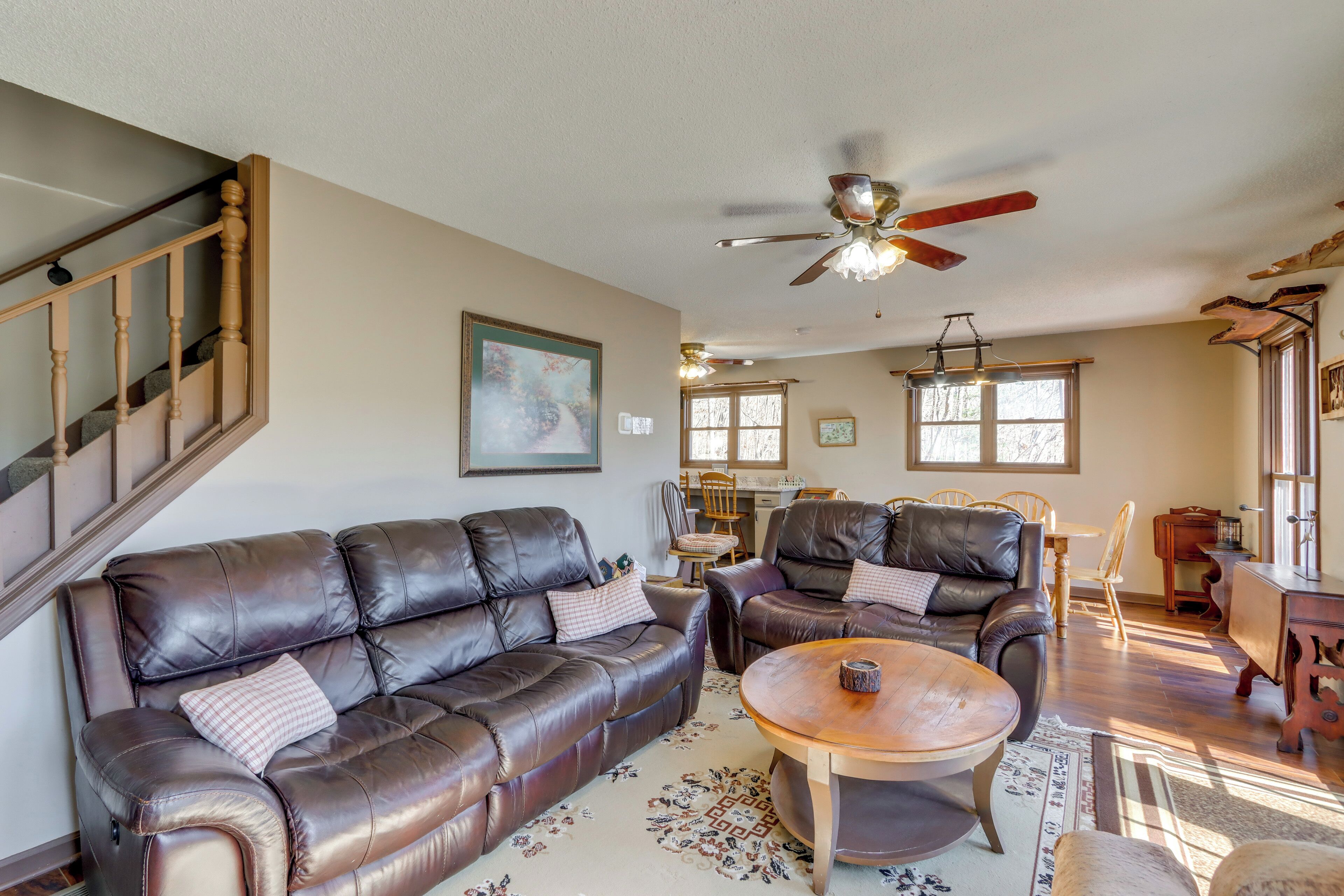 A spacious living room with a brown leather sofa, a wooden coffee table, and a ceiling fan.