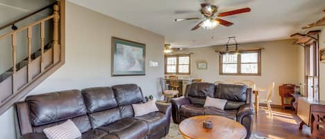A spacious living room with a brown leather sofa, a wooden coffee table, and a ceiling fan.