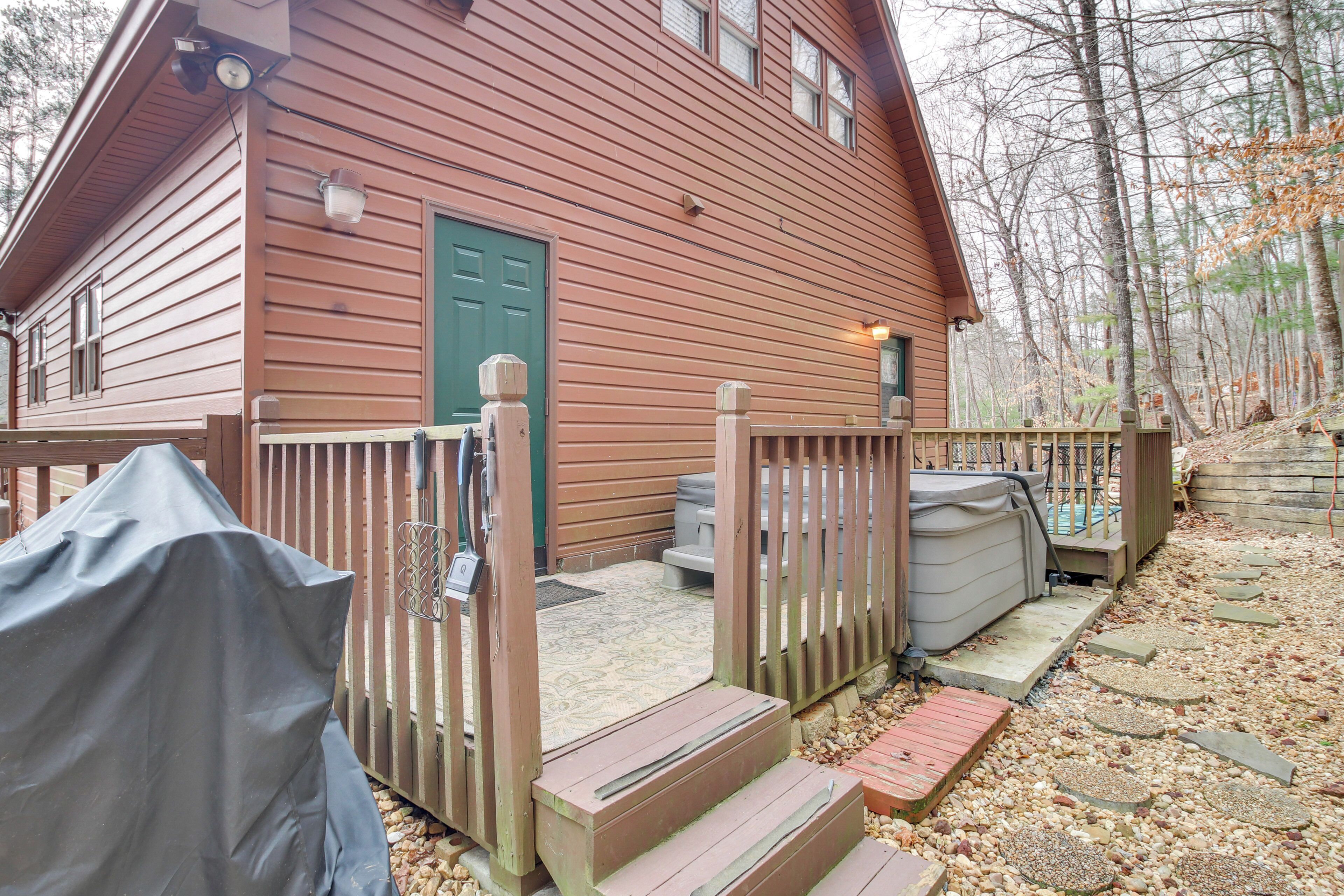 A wooden cabin with a green door, a covered porch, and a hot tub.