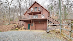 Une cabane en bois à deux étages, dotée d’un balcon, d’un garage et d’une allée gravillonnée.