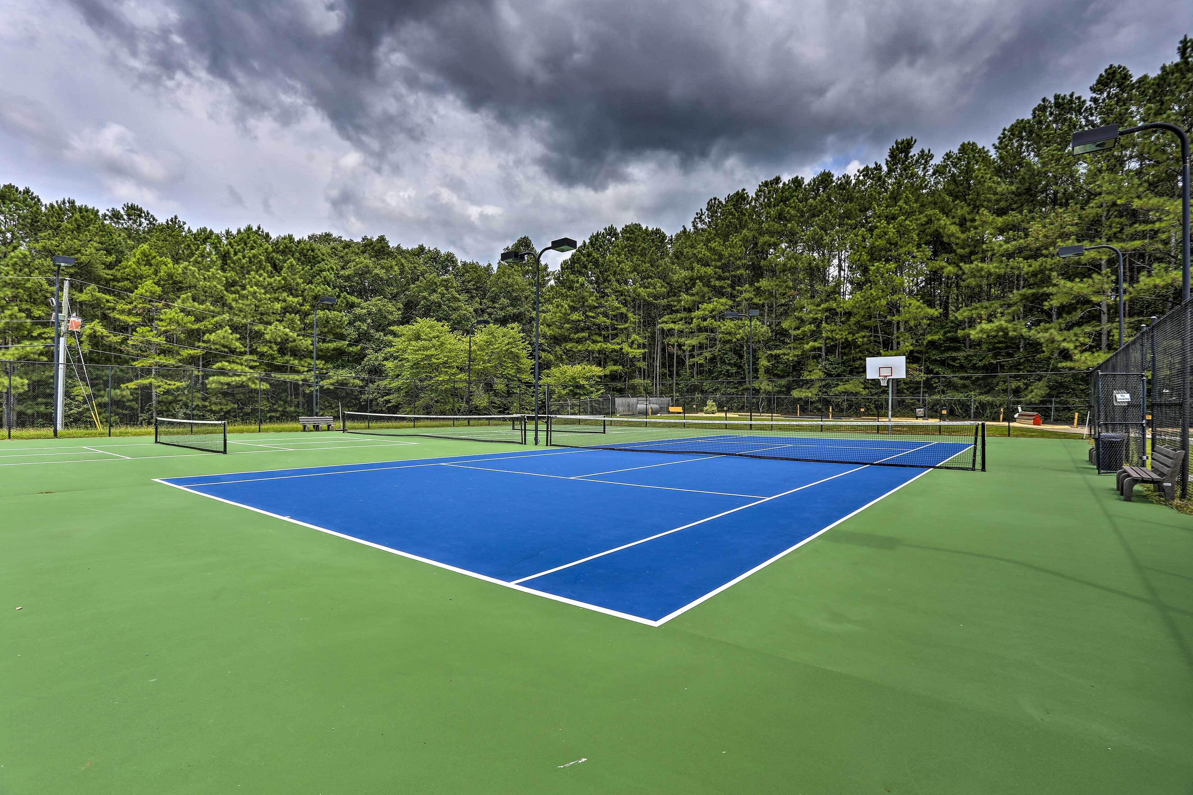 Un terrain de tennis avec un filet, entouré d’arbres et agrémenté d’un panier de basket.