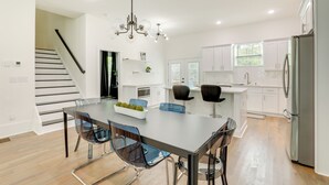 A modern kitchen with white cabinets, a stainless steel refrigerator, and a dining area with a glass table and chairs. - Modern Decatur Home ~ 7 Mi to Atlanta! (Decatur)