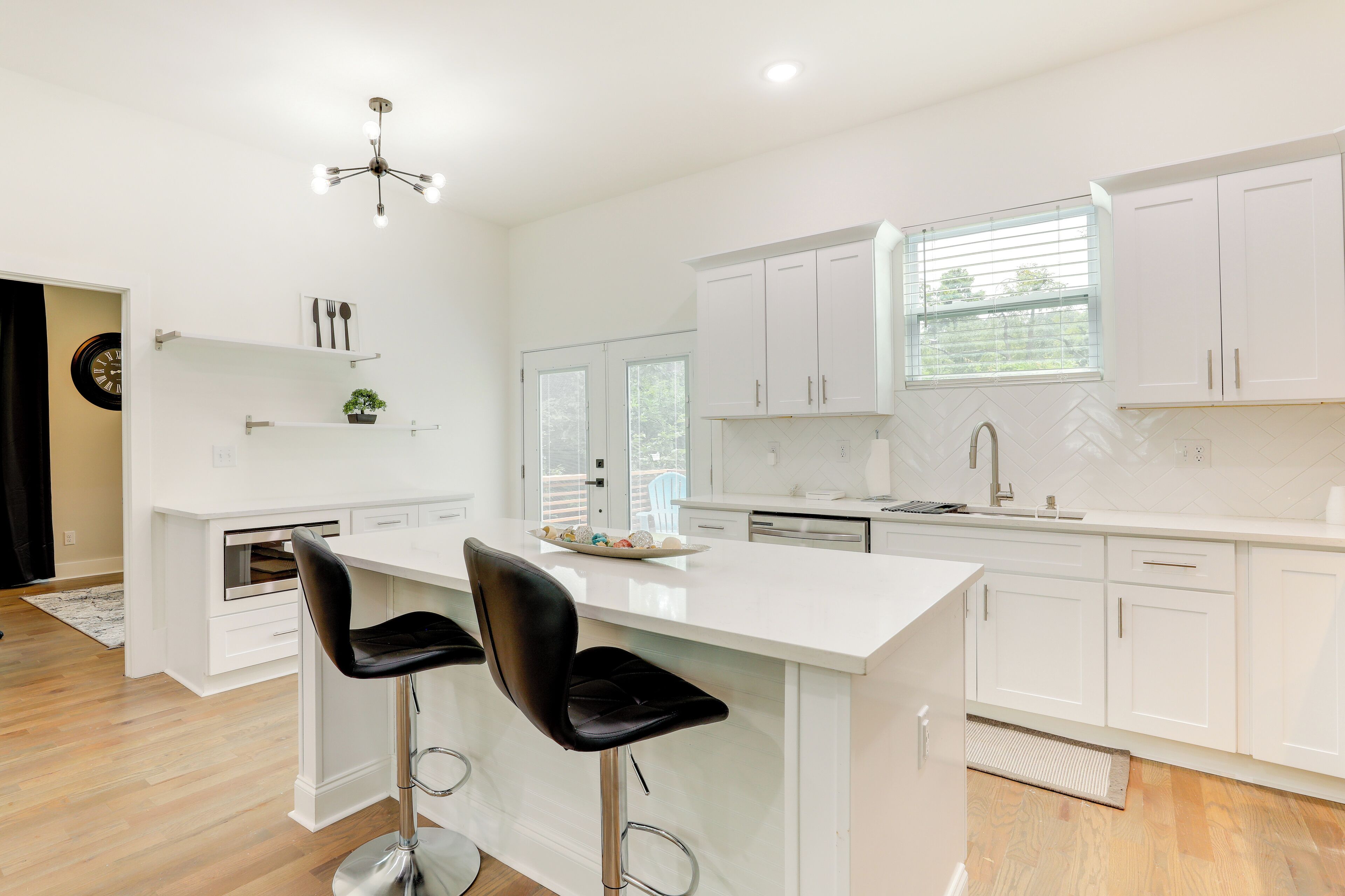 A modern kitchen with white cabinetry, a central island with two bar stools, a built-in oven, and a window providing natural light.