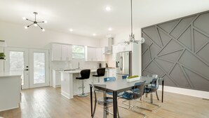 A modern kitchen with white cabinets, a central island, and a dining area with clear chairs. - Modern Decatur Home ~ 7 Mi to Atlanta! (Decatur)