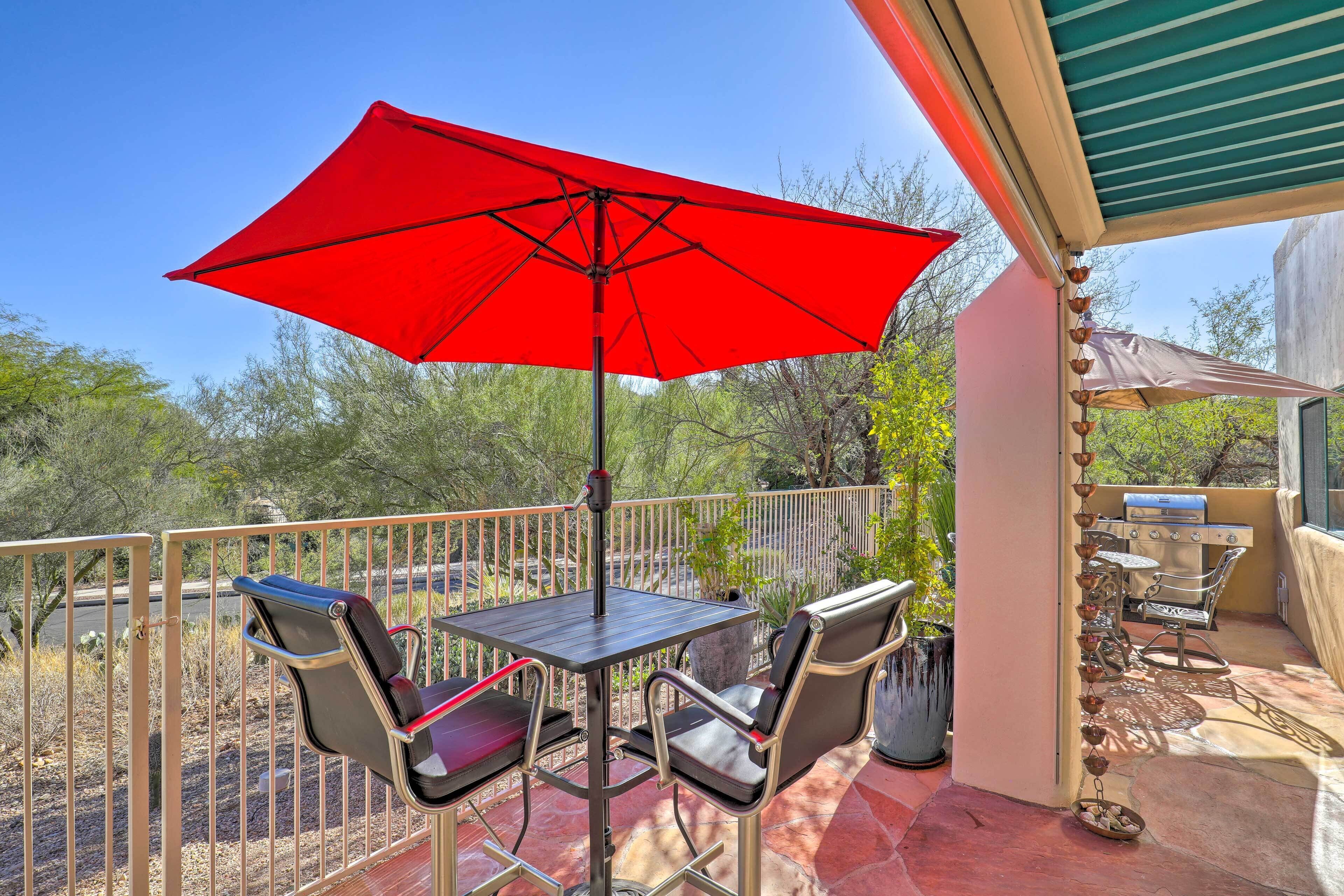Une terrasse avec une table et des chaises, un parasol rouge et un barbecue.