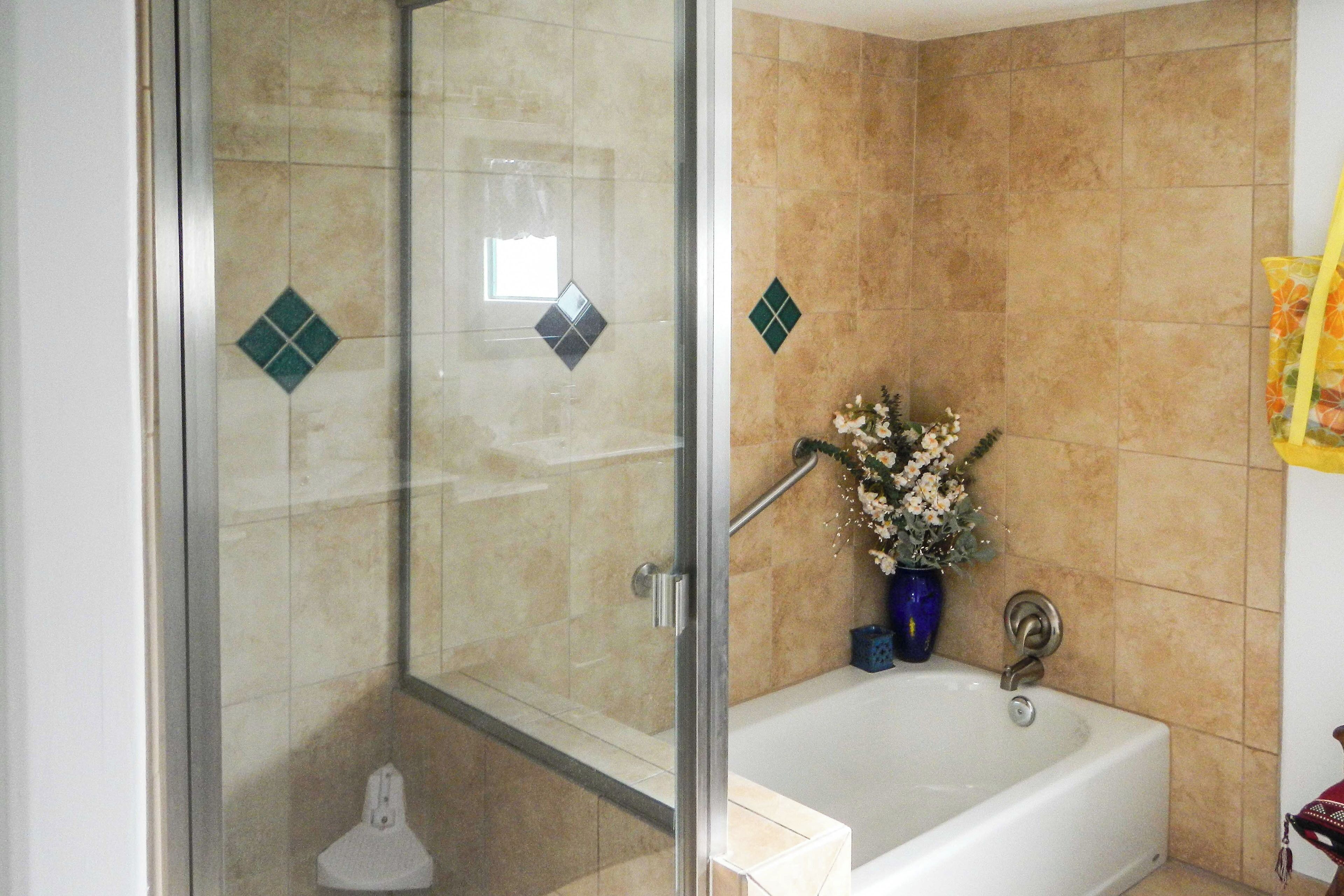 Ein Badezimmer mit einer Glaskabine zur Dusche, einer weißen Badewanne und einer blauen Vase mit Blumen.