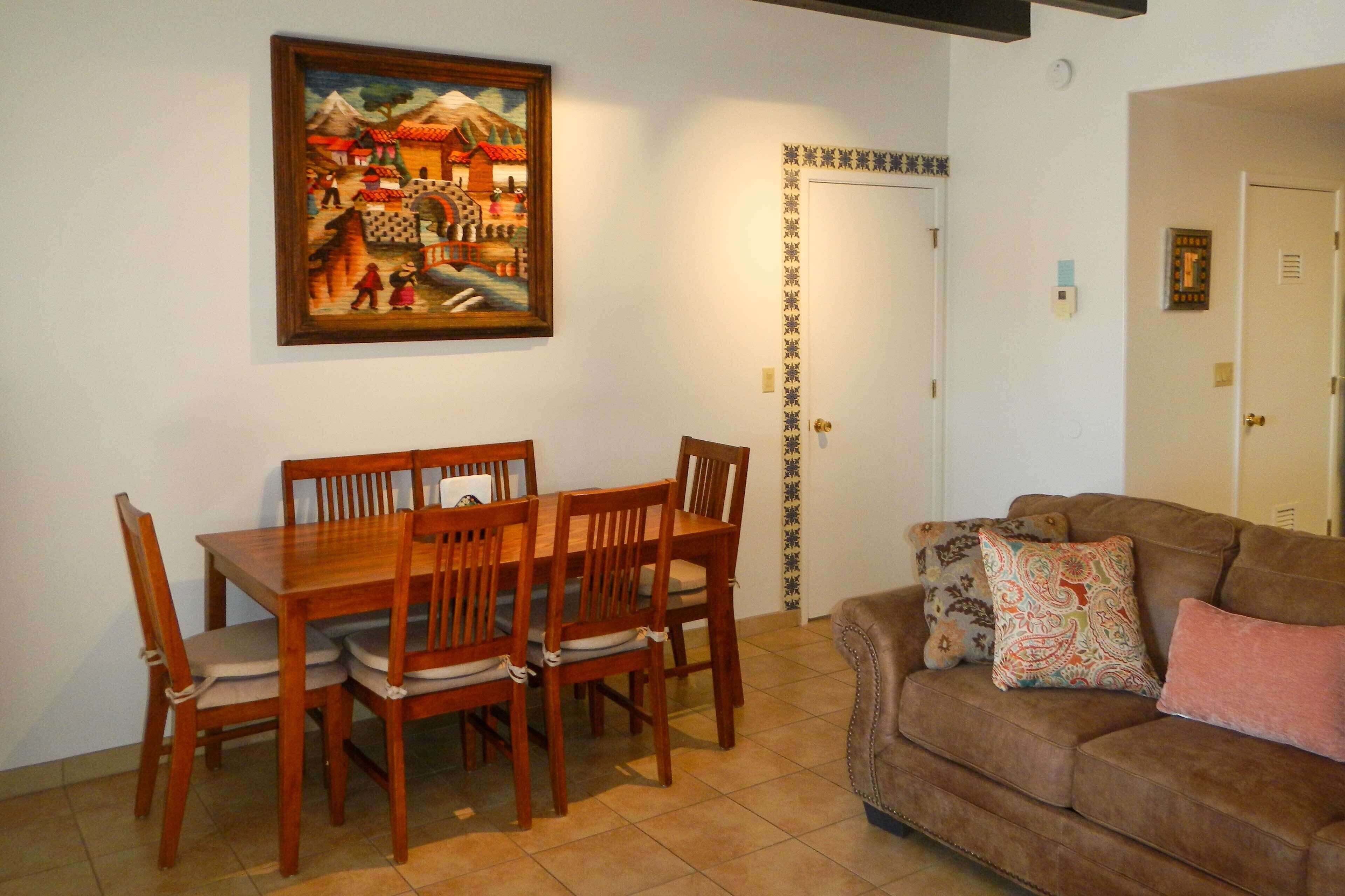A dining area with a wooden table and chairs, a painting on the wall, and a brown sofa with decorative pillows.