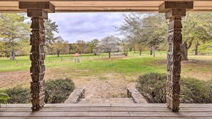 A covered outdoor area with ornate wooden columns and a view of a park with trees and a gazebo. - Charming Retreat on 80-acre Willow Rock Ranch! (Woodbury)