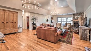 A spacious living room with hardwood floors, a large brown leather sofa, a fireplace, and two chandeliers. - Charming Retreat on 80-acre Willow Rock Ranch! (Woodbury)