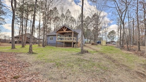 A cabin with a covered porch, surrounded by trees and a grassy yard. - Creek-view Getaway w/ Deck, Yard, & Fire Pit! (Summerville)