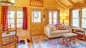 A cozy cabin interior with a wooden door, a sofa, a table, and a rug. - 'little Fox Den Ellijay Cabin Rental w/ Hot Tub! (Ellijay)