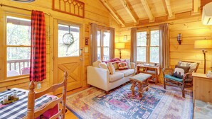 A cozy cabin interior with a wooden ceiling, a white sofa, a patterned rug, and a dining table with chairs. - 'little Fox Den Ellijay Cabin Rental w/ Hot Tub! (Ellijay)