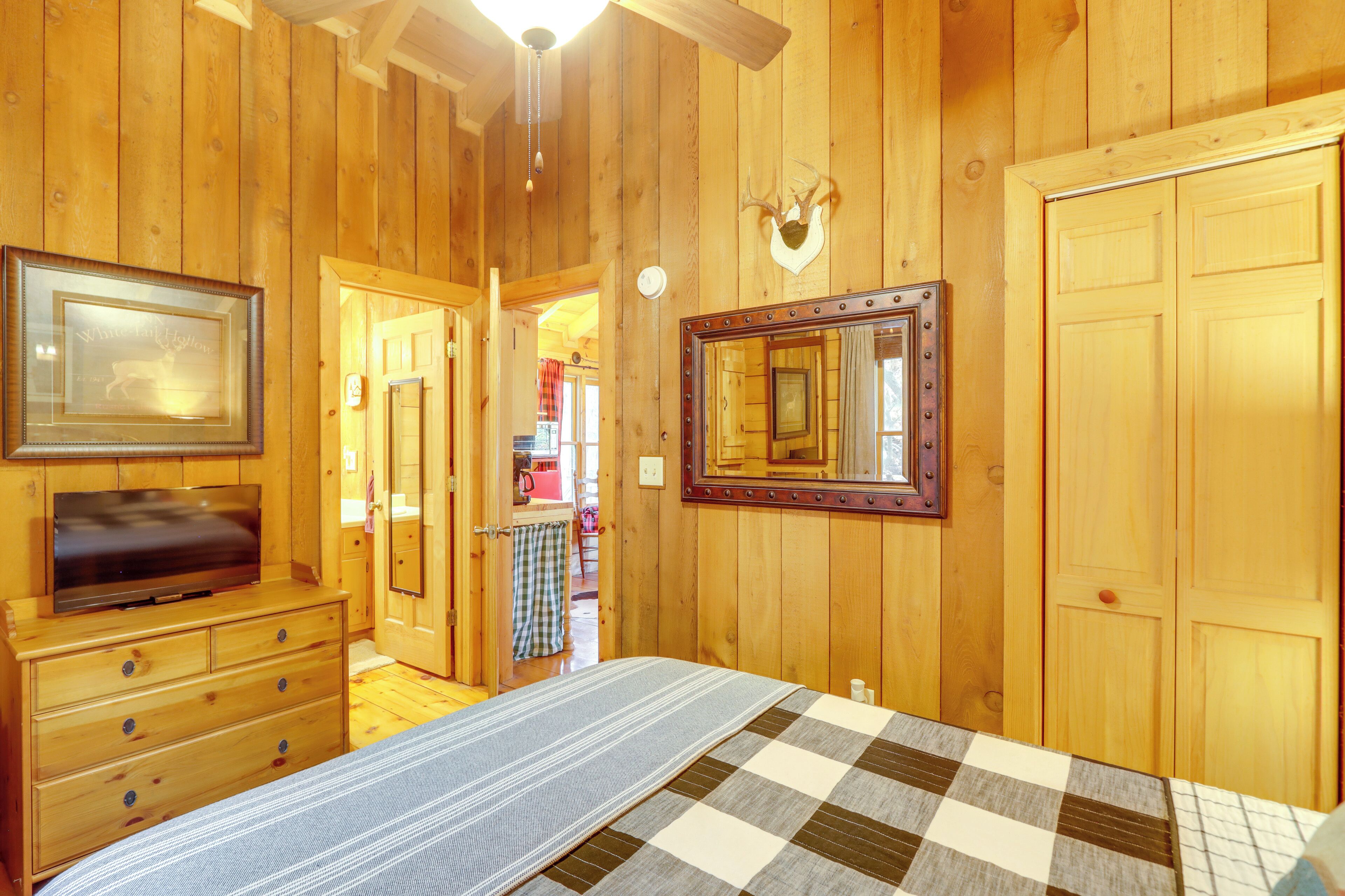 Una habitación con paneles de madera, con cama, cómoda, televisor y espejo.