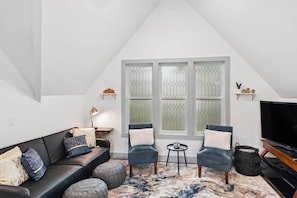 A modern living room with a black leather sofa, two armchairs, a TV, and a large window with decorative glass panes.