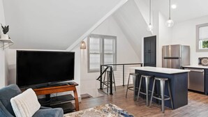 A modern living room with a flat-screen TV, a comfortable sofa, and a dining area with stools. - Nashville Vacation Rental Near Bridgestone Arena! (Nashville)