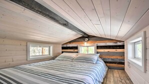 A bedroom with a large bed, wooden walls, and two windows. - Blairsville Tiny Home w/ Covered Furnished Deck! (Blairsville)