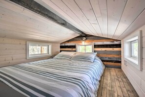 A bedroom with a large bed, wooden walls, and two windows. - Blairsville Tiny Home w/ Covered Furnished Deck! (Blairsville)