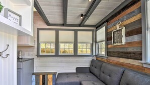 A cozy interior with a sectional sofa, wooden beams, and a large window with blinds. - Blairsville Tiny Home w/ Covered Furnished Deck! (Blairsville)