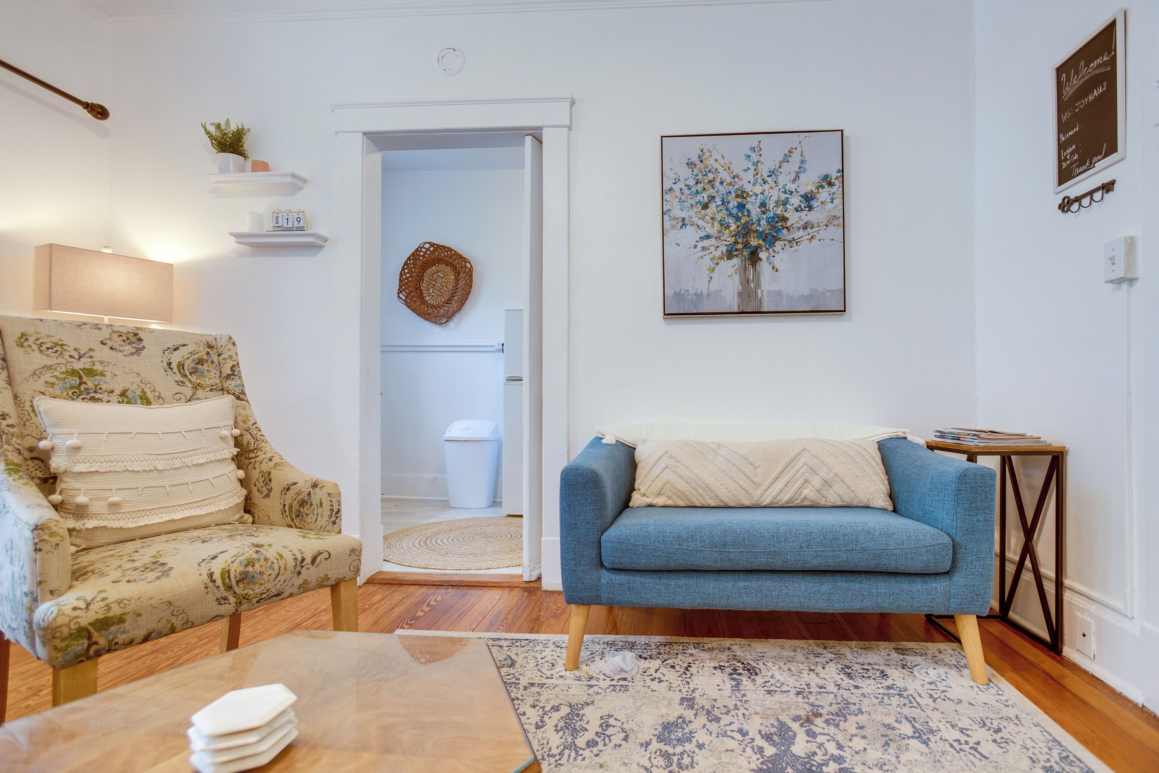A living room with a floral armchair, a blue sofa, a wooden coffee table, and a patterned rug.