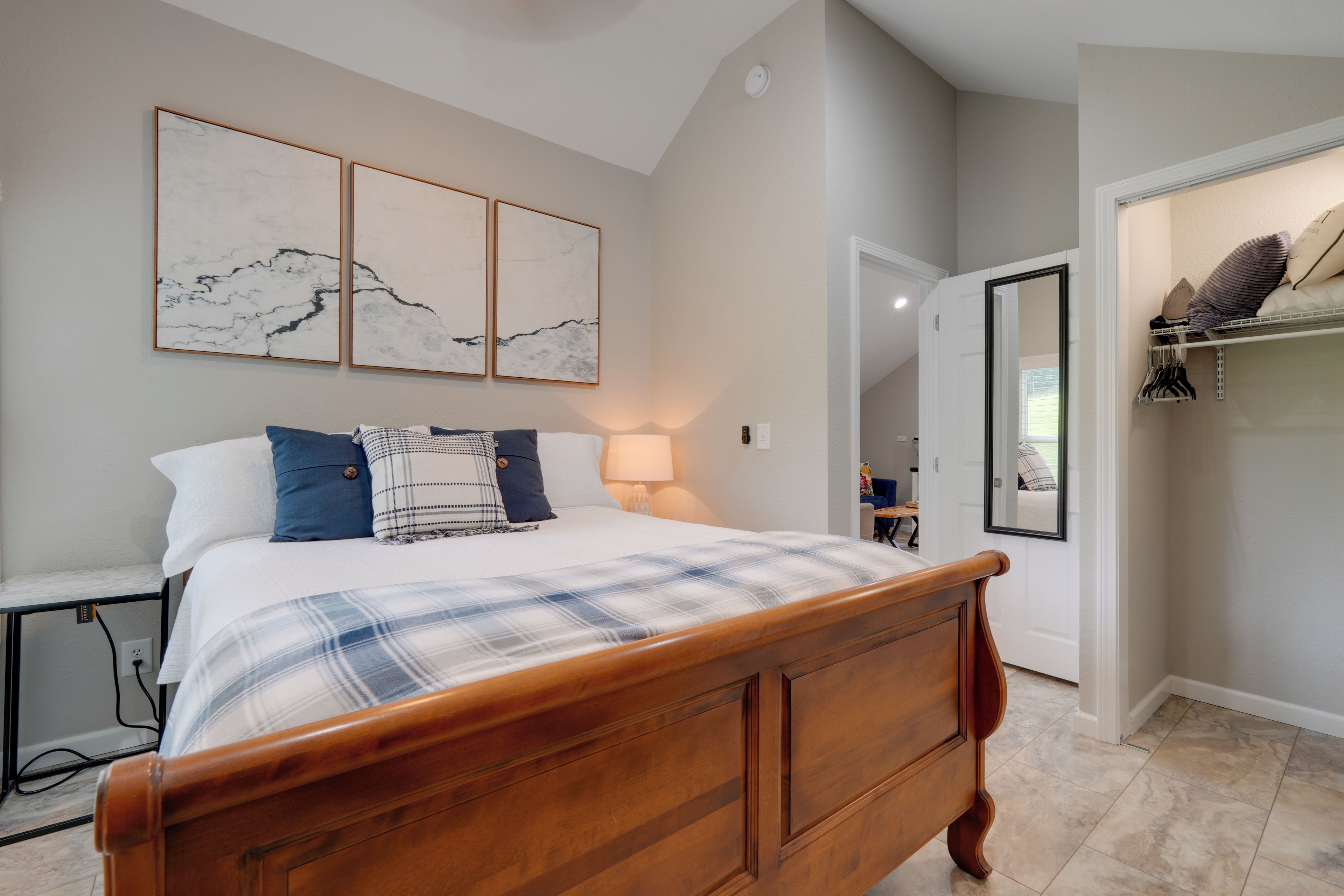 A bedroom with a wooden bed, a bedside table, a lamp, and a wall-mounted mirror.