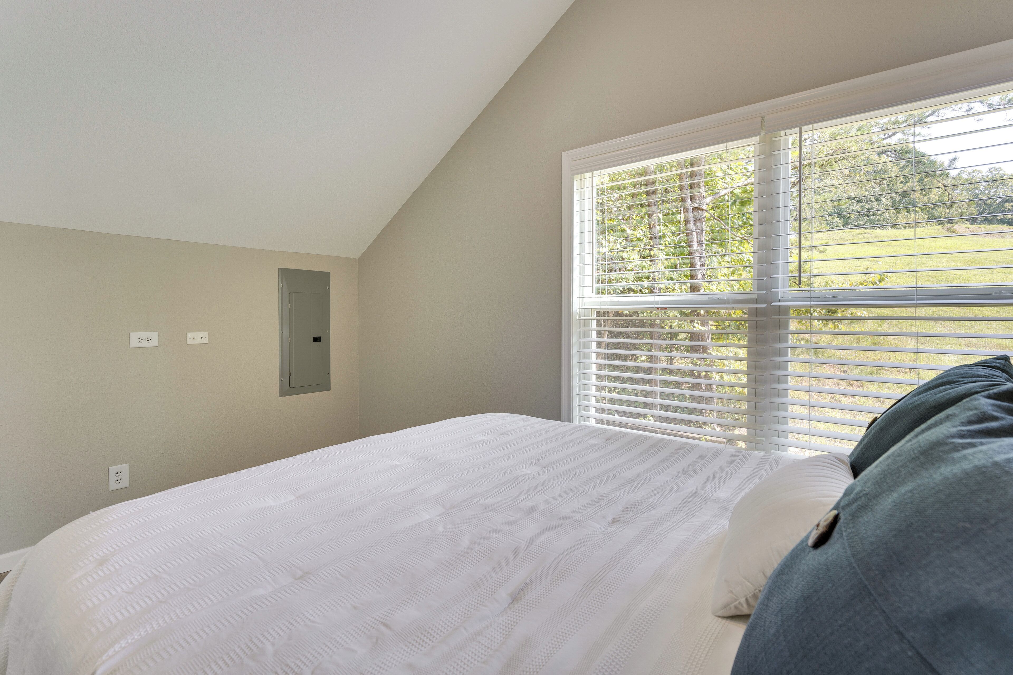 Une chambre à coucher avec un lit, une fenêtre avec des stores et un petit coin avec un miroir.