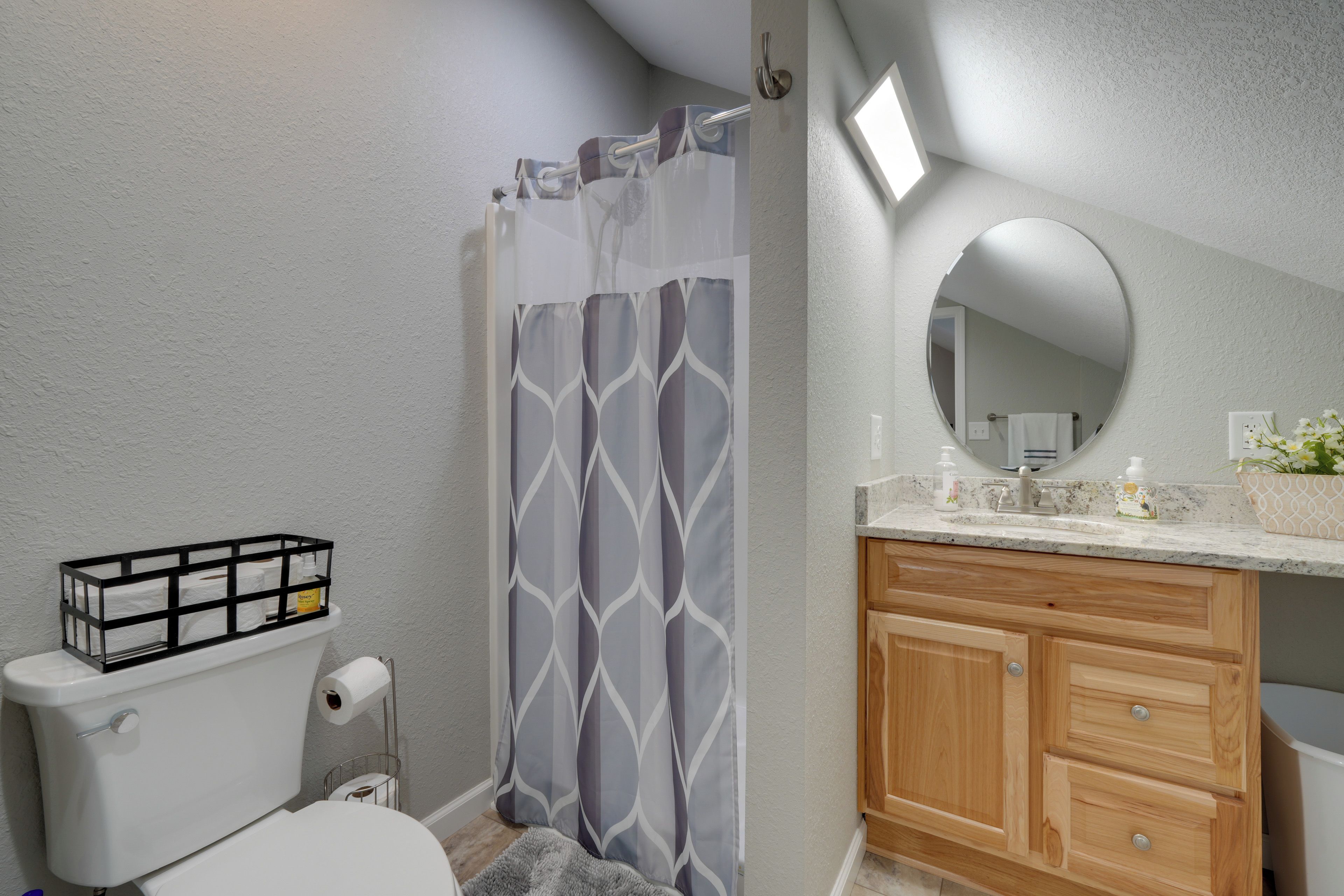 A bathroom with a toilet, a shower curtain, a vanity with a mirror, and a sink.