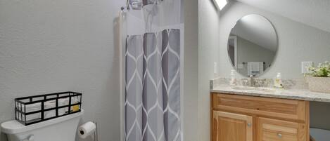 A bathroom with a toilet, a shower curtain, a vanity with a mirror, and a sink.