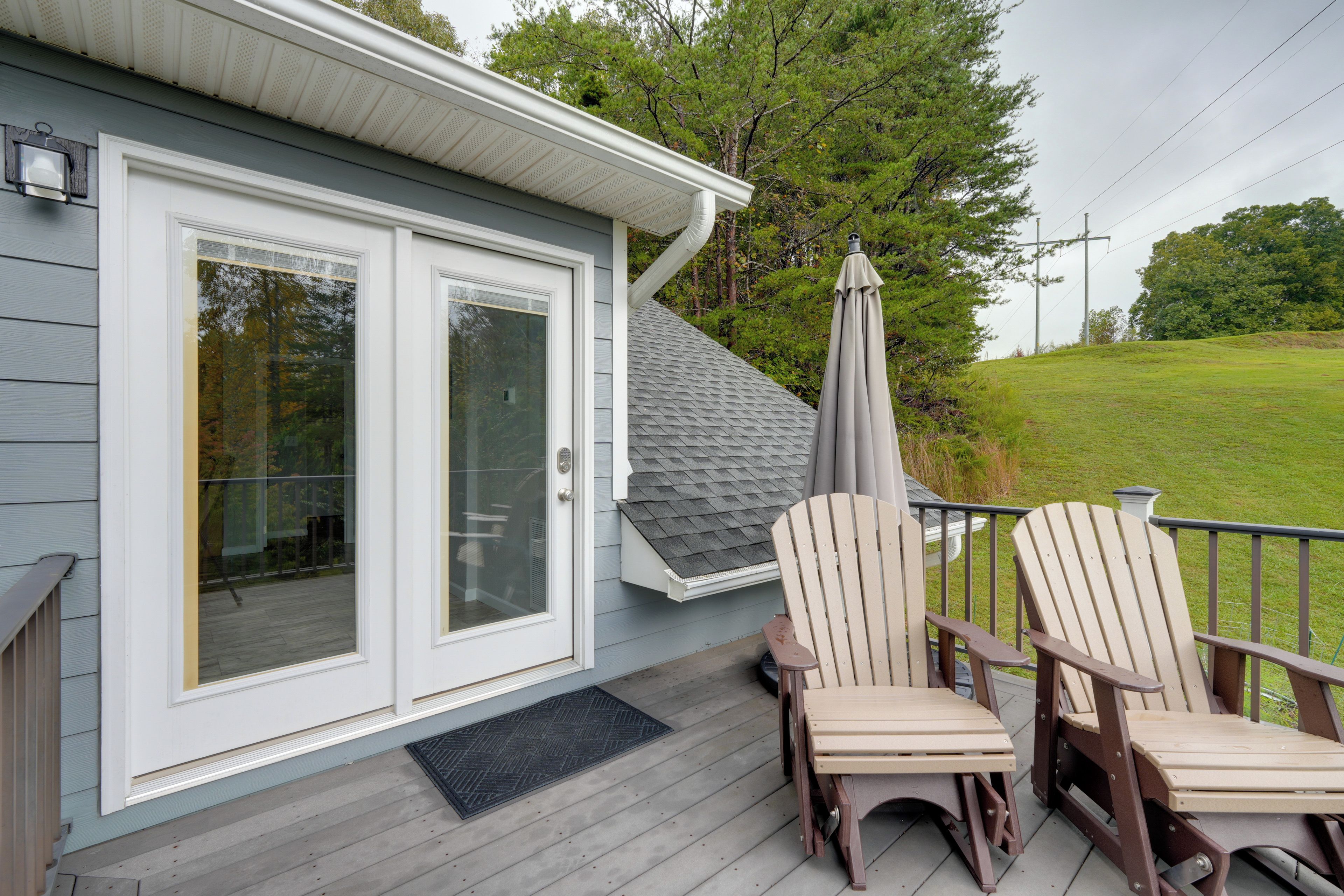 A deck with two Adirondack chairs, a glass door, and a grey roof.
