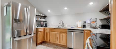 A modern kitchen with stainless steel appliances, wooden cabinets, and a tiled floor.