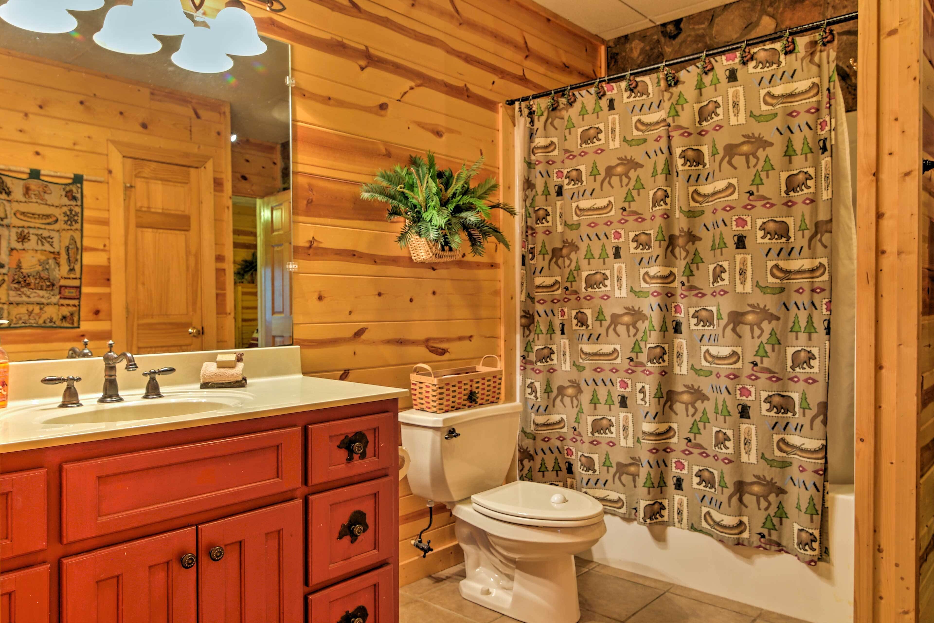 A bathroom with wooden walls, a white toilet, a sink with a mirror, and a shower curtain with a wildlife print.