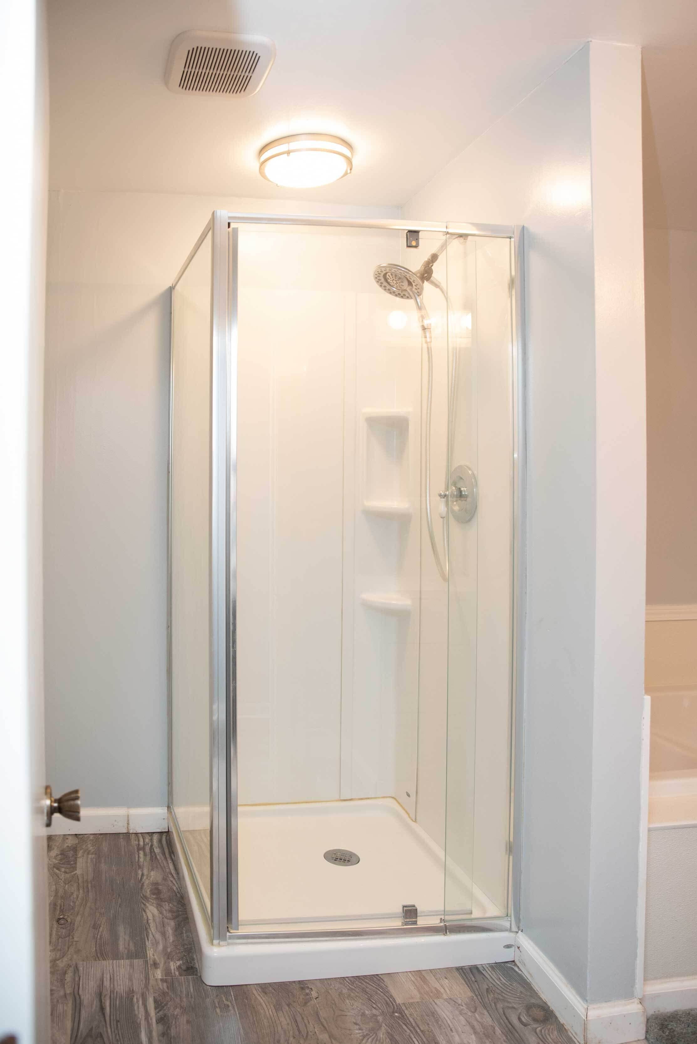A glass-enclosed shower with a built-in shelf and a ceiling light fixture.