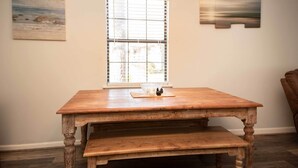 A wooden dining table with a bench, a window with blinds, and two wall-mounted artworks. - Lakefront Cottage w/ Private Hot Tub! (Buckhead)