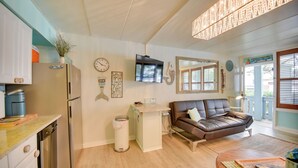 A compact living space with a kitchenette, a flat-screen TV, a brown leather sofa, and a dining area with a wooden table. - Chic Virginia Beach Retreat - Pool, Steps to Beach (Virginia Beach)