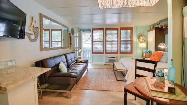A cozy living room with a brown leather sofa, a wooden dining table, and a kitchen area with a countertop and cabinets. - Chic Virginia Beach Retreat - Pool, Steps to Beach (Virginia Beach)