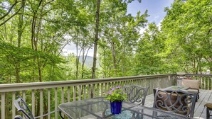 Une terrasse dotée d’une table et de chaises en verre, entourée d’une rambarde en bois, et offrant une vue sur une zone boisée.