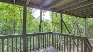 Une terrasse en bois couverte, dotée de rampes de protection, qui offre une vue sur une zone boisée.