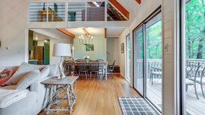 Un vaste espace de vie doté d’un haut plafond, une table à manger avec des chaises, un canapé et un escalier menant à un niveau supérieur.
