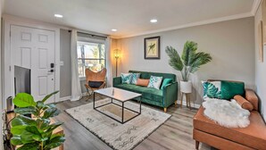 A living room with a green sofa, a brown leather chair, a white coffee table, and a large plant. - Private Yard + Fire Pit: Commerce Home! (Commerce)