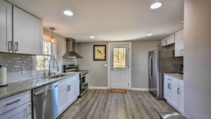 A modern kitchen with stainless steel appliances, white cabinets, and a wooden floor. - Private Yard + Fire Pit: Commerce Home! (Commerce)